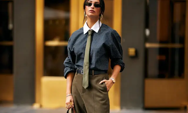 Donna con un audace outfit con cravatta, camicia a quadri, pantaloni kaki e borsa di lusso.
