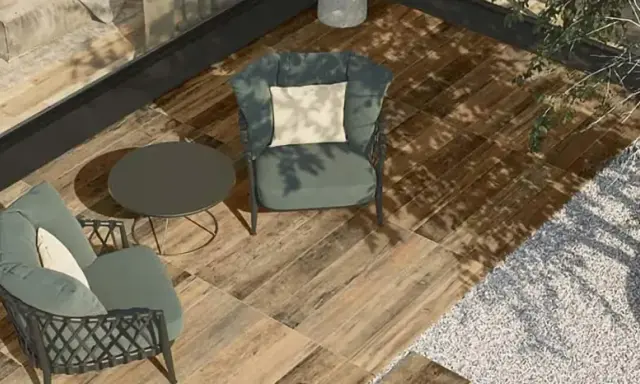 Aménager une terrasse moderne avec des fauteuils confortables, une table basse et un sol imitation bois. L'ombre des arbres crée une atmosphère paisible.
