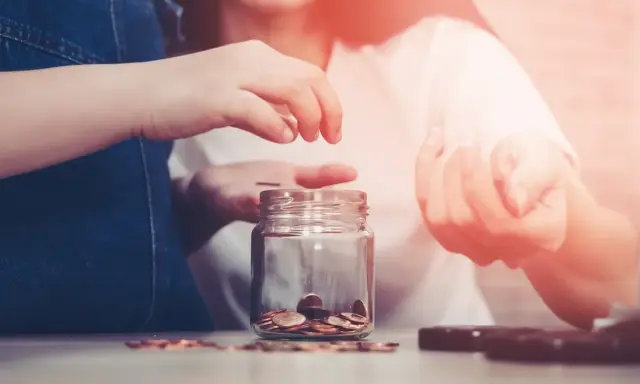 Dwie osoby wrzucają monety do słoika, oszczędzając na przyszłość. Zastanawiasz się, ile wynoszą alimenty na studenta?