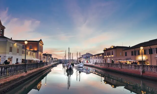 Canale di Cesenatico al tramonto, con barche a vela ormeggiate e riflessi sull'acqua. La riviera cesenatico incanta con i suoi colori.