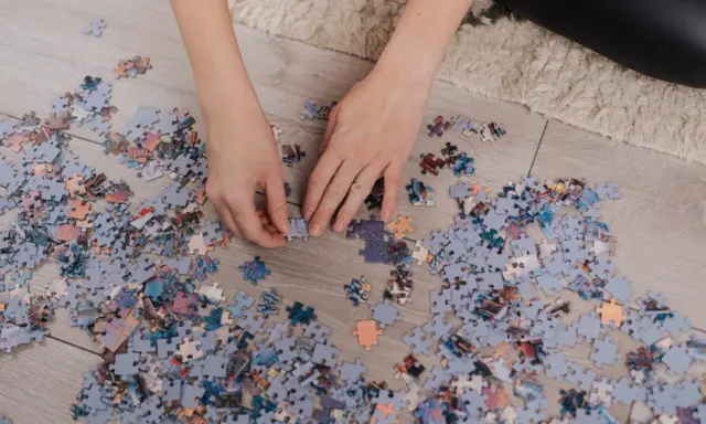 Ręce układają puzzle na podłodze. Po skończeniu dowiesz się, jak powiesić puzzle na ścianie.