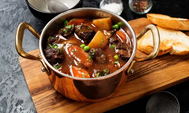 Herzhaftes Chili con Carne in Kupfertöpfchen, mit Kartoffeln, Karotten und Erbsen, serviert mit Baguette.