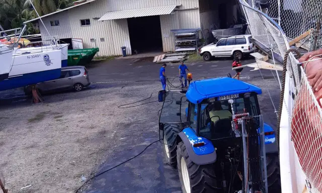 Tracteur bleu près d'un bateau, peut-être pour le prix d'entretien d'un bateau de 7m. Des ouvriers travaillent.