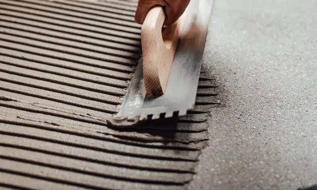 Application d'enduit pour carrelage avec une taloche crantée, assurant une épaisseur carrelage et colle uniforme pour une pose parfaite.