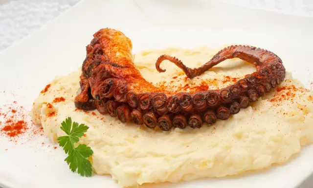 Delicioso pulpo a la plancha con puré cremoso, espolvoreado con pimentón y adornado con perejil fresco.