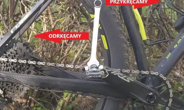 Klucz do pedałów rowerowych przy korbie, z czerwonymi strzałkami wskazującymi "Odkręcamy" i "Przykręcamy".
