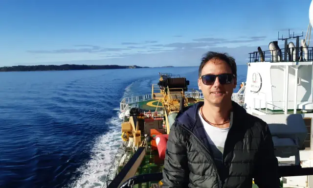 Uomo su nave, con mare e terra all'orizzonte. Un vero oceanografo significato, immerso nella sua ricerca.