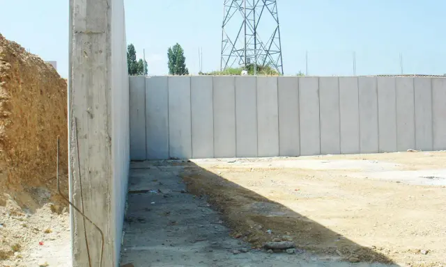 Construcción de muros de contención de hormigón prefabricados, con una torre de alta tensión al fondo.