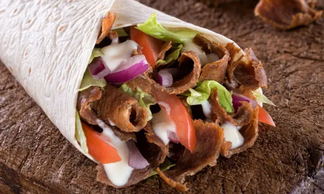Pyszny, domowy kebab zawinięty w tortillę z soczystym mięsem, chrupiącą sałatą, pomidorami i cebulą, polany sosem.