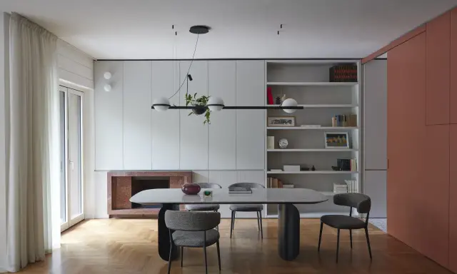 Sala da pranzo moderna con tavolo ovale, sedie imbottite e libreria a giorno. Le pareti grigio luminoso creano un'atmosfera sofisticata.