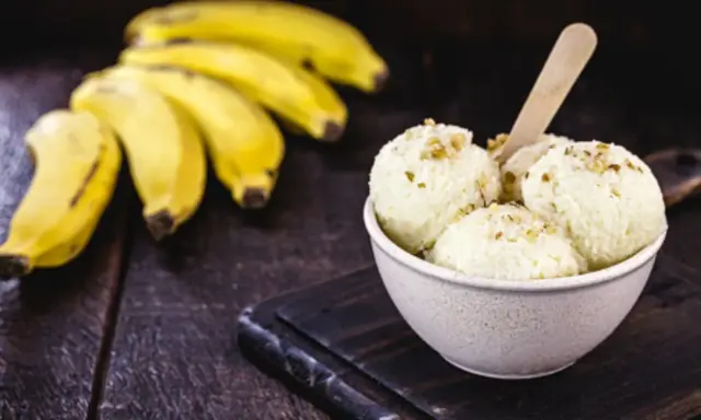 Delicioso helado de plátano cremoso, adornado con nueces, junto a racimos de plátanos frescos sobre una mesa de madera rústica.