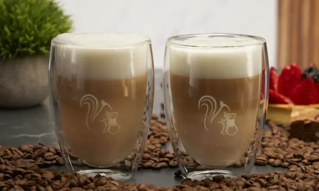 Zwei Latte Macchiato im Glas, umgeben von Kaffeebohnen. Ein typischer Latte Macchiato hat ca. 250-300 ml.