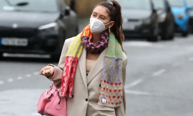 Iris Law, con mascarilla y bufanda multicolor, camina por la calle con un bolso rosa.