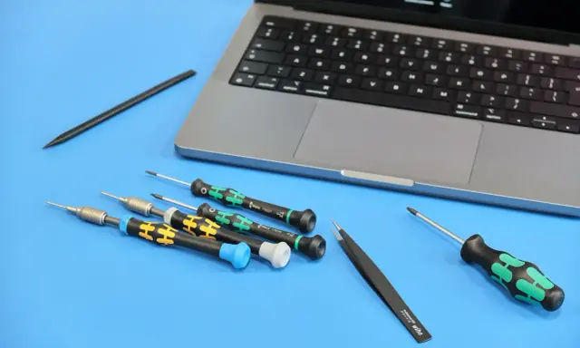 Narzędzia do naprawy iPhone'a: precyzyjne śrubokręty i pęseta obok laptopa. Przygotowanie do serwisu.