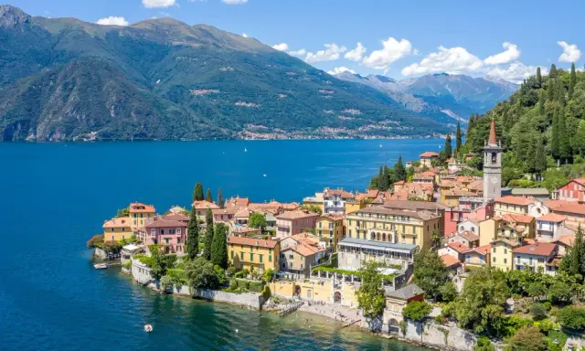 Färgstarka hus vid en azurblå sjö, omgivna av gröna berg. Ett perfekt exempel på mysiga resmål i Italien.