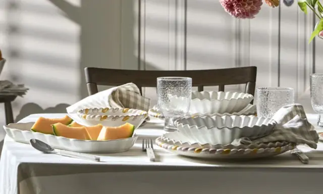 Ett dukat bord med en fin servis, frukt och blommor. Vackra vita skålar med vågiga kanter och glas med textur.