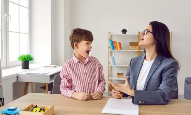 Chłopiec z otwartymi ustami wykonuje ćwiczenia podniebienia miękkiego z logopedą.