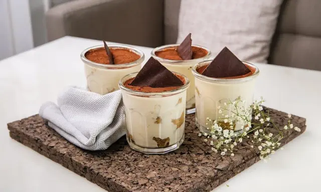 Quatre verrines de tiramisu, garnies de cacao et d'une feuille de chocolat. Une serviette grise et des petites fleurs blanches décorent le plateau en liège. Pourquoi mon tiramisu est liquide ?