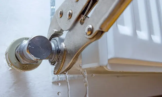 Herramienta sujetando una conexión de radiador mientras gotea agua. Guía visual para como quitar un radiador.
