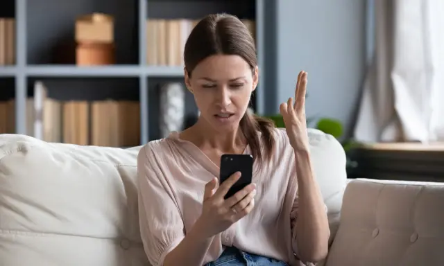 Zirytowana kobieta próbuje włączyć internet w telefonie, gestykulując z frustracją.