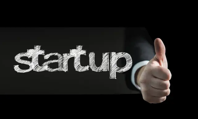 Słowo "startup" napisane kredą na czarnym tle, obok kciuk w górę. To symbol sukcesu w biznesie.