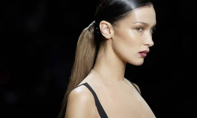 Bella Hadid luce un elegante peinado de cola de caballo con pelo efecto mojado, resaltando su perfil y maquillaje.