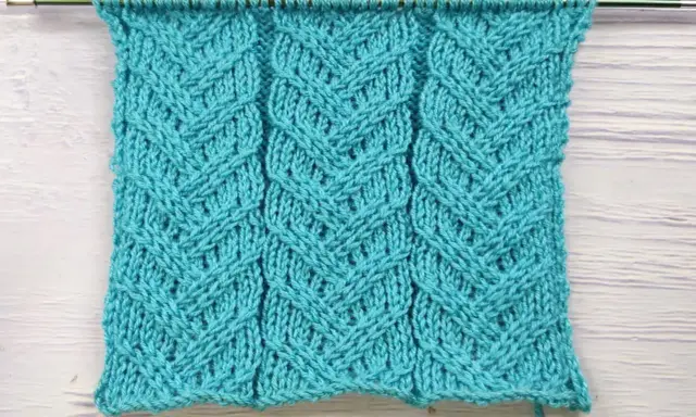 Muestra de tejido azul turquesa con patrón de espiga en dos agujas. Las hebras forman un diseño entrelazado que recuerda a espigas de trigo.