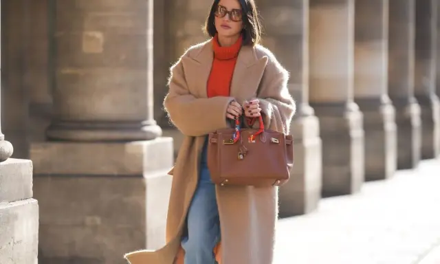 Elegancka kobieta w płaszczu i pomarańczowym golfie, prezentująca modne mom jeans stylizacje zima. Brązowa torebka dodaje szyku.