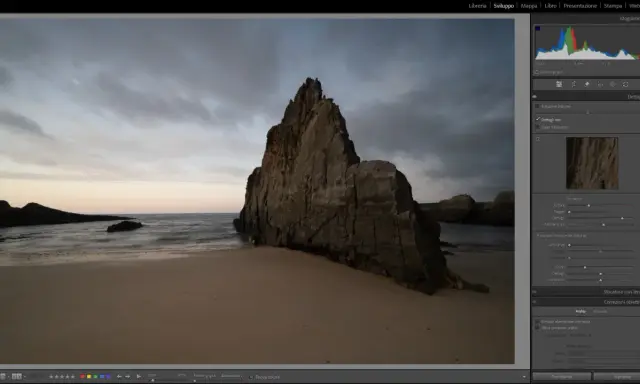 Scogliera imponente su una spiaggia al tramonto, con onde mosse. L'aggiornamento Lightroom sta migliorando i dettagli dell'immagine.