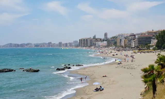 Sonniger Benalmadena Strand mit vielen Menschen, bunten Sonnenschirmen und dem türkisfarbenen Meer.
