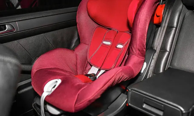 Silla de coche roja en asiento de cuero negro. Las sillas Isofix se pueden poner con cinturón, ofreciendo versatilidad para la seguridad infantil.