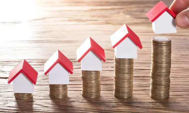 Cinq maisons miniatures sur des piles de pièces, symbolisant une augmentation du loyer sur 3 ans.