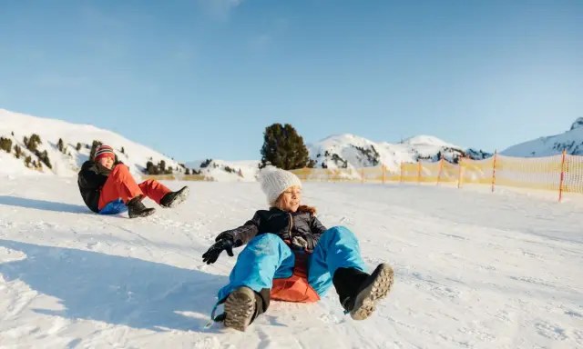 Bambini felici scendono con slittino su pendio innevato. L'altitudine neonati non è un problema per queste avventure invernali.