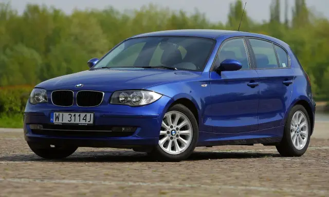 Niebieskie BMW 118i na tle zieleni. Elegancki hatchback z polskimi tablicami rejestracyjnymi WI 3114J.
