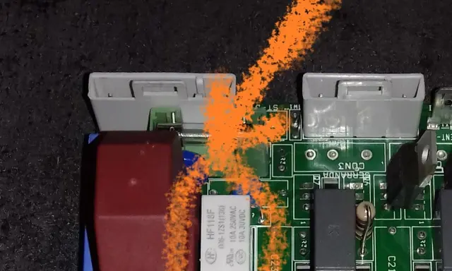 Carte mère de poêle à granulés avec un problème. On voit des connecteurs, des composants électroniques et une trace orange.
