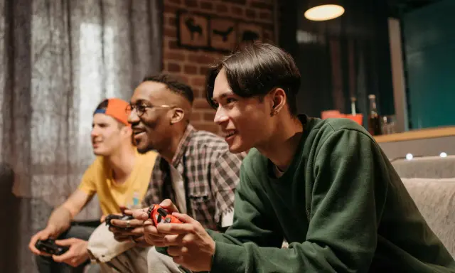 Trzech przyjaciół gra w darmowe gry na PS4, śmiejąc się i rywalizując.