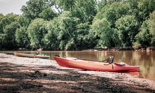 Dwa kajaki na brzegu rzeki na Podlasiu, otoczone bujną zielenią drzew.