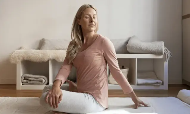 Kvinna i rosa tröja och grå byxor gör en vridning i sittande ställning, en form av gående meditation.