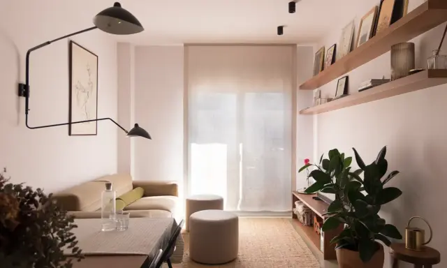 Salón moderno con sofá beige, mesa y dos pufs. Las paredes lucen un impecable **microcemento acabado**, aportando elegancia y minimalismo.