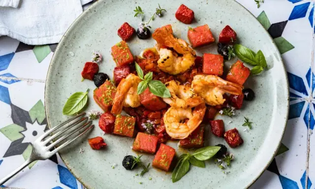 Saftige argentinische Rotgarnelen mit Wassermelonenwürfeln, Tomaten und Basilikum auf einem Teller.