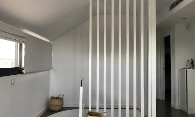 Modern interior with a white slatted partition, possibly to tirar tabique para unir dos pisos. Baskets and a window are visible.