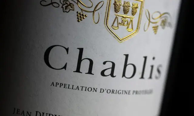 Nahaufnahme eines Etiketts mit der Aufschrift "Chablis". Ein goldenes Wappen mit Trauben und Waage ziert das Etikett dieses Chablis Weins.