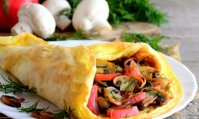 Złocisty omlet z pomidorami i pieczarkami, udekorowany koperkiem. Pyszne śniadanie na drewnianym blacie.