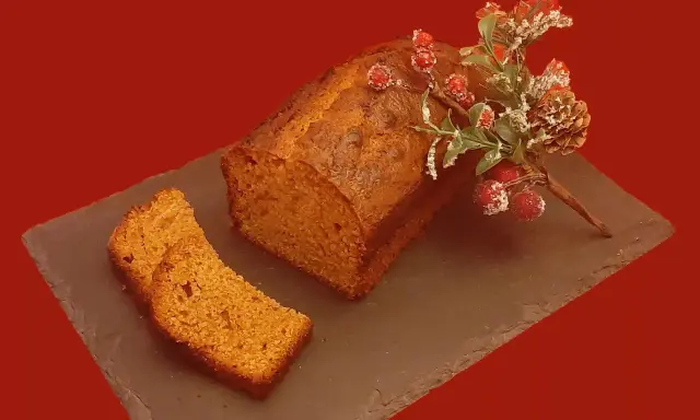 Un délicieux pain d'épice, décoré de baies rouges et de branches givrées, est prêt à être dégusté. Une tranche est déjà coupée.