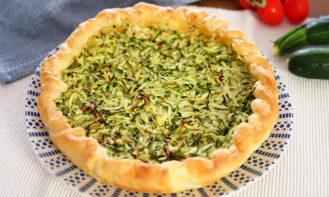 Torta salata con zucchine grattugiate e ricotta, con bordo dorato e decorazione blu su piatto bianco.