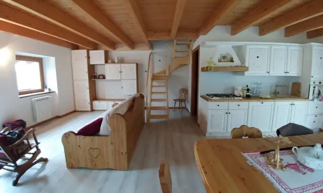 Come arredare una taverna: cucina bianca, divano in legno, scala a vista e soffitto a travi.
