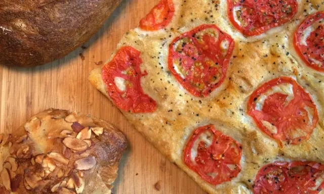 Focaccia receta con tomates frescos y hierbas, junto a un pan rústico y un bollo con almendras.