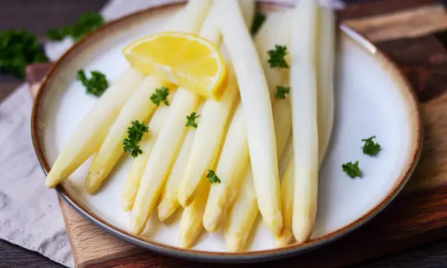 Frischer weißer Spargel, perfekt gekocht, garniert mit Petersilie und einer Zitronenspalte auf einem Teller. Ein Genuss, der Lust auf mehr macht.