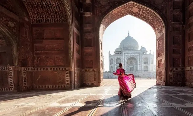Una mujer con un sari rosa vibrante baila bajo un arco, revelando el Taj Mahal. Descubre curiosidades del Taj Mahal.