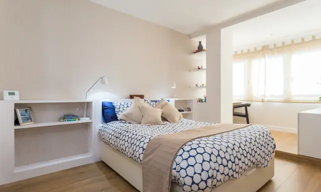 Habitación moderna con cama, estanterías y una apertura que permite tirar tabique para unir dos habitaciones.